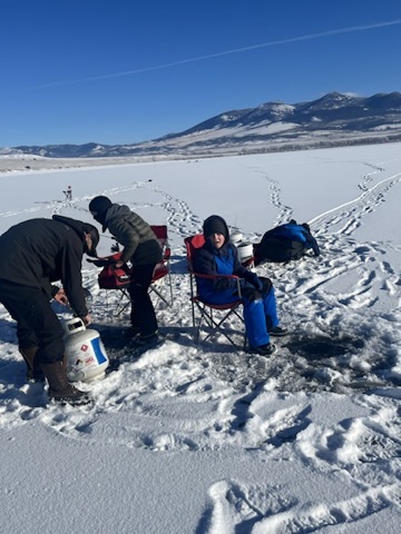 Church members ice fishing together on a frozen lake with the Bridger Mountains in the background