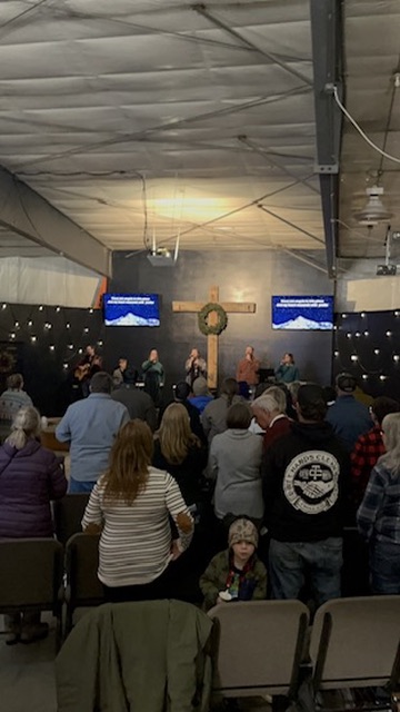 Congregation standing in worship beneath the cross during a Sunday evening service